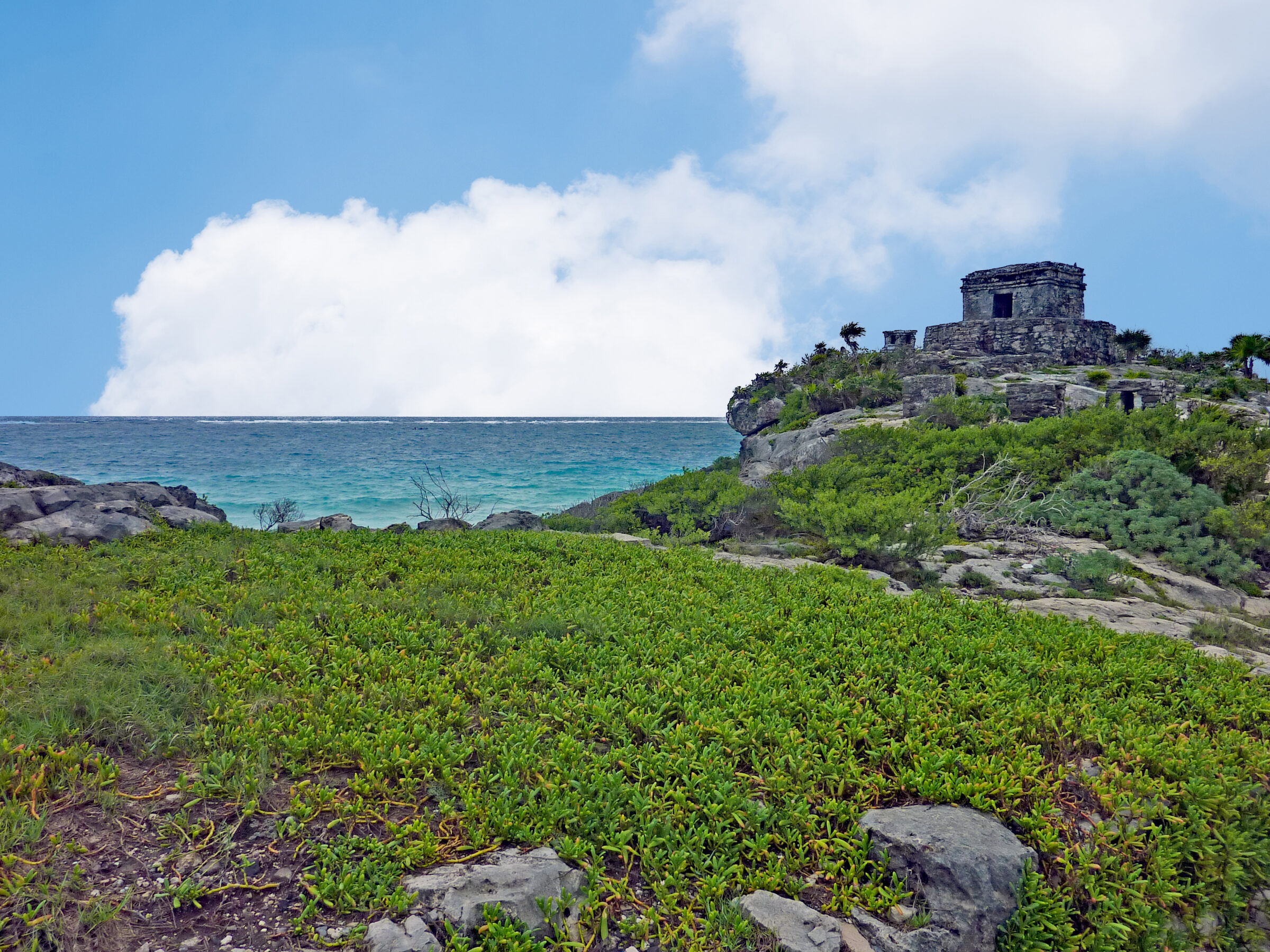 Ruines du site archéologique de Tulum surplombant la mer des Caraïbes, sous un ciel légèrement nuageux, sans visiteurs.